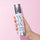 Hand holding a silver and white bottle labeled 'Color WOW' against a pink background